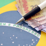 Bandeira do Brasil com notas de real e caneta, simbolizando finanças e progresso.
